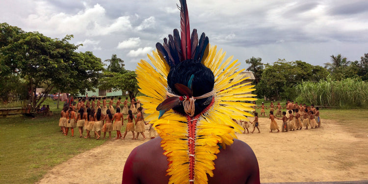 Yawanawá man wearing a traditional yellow feather headdress with red and black accents during a village ceremony in the Amazon.