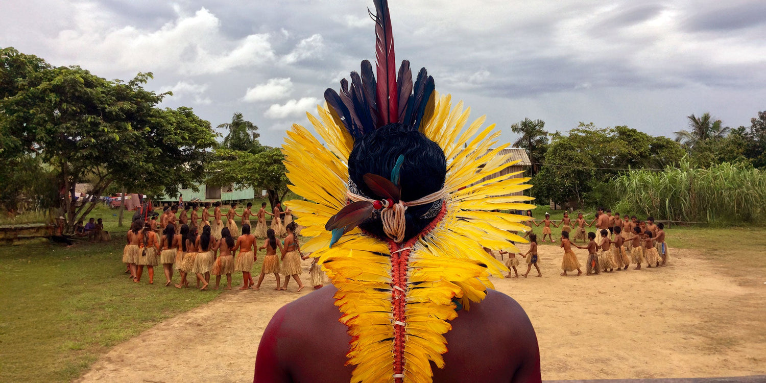 Yawanawá man wearing a traditional yellow feather headdress with red and black accents during a village ceremony in the Amazon.