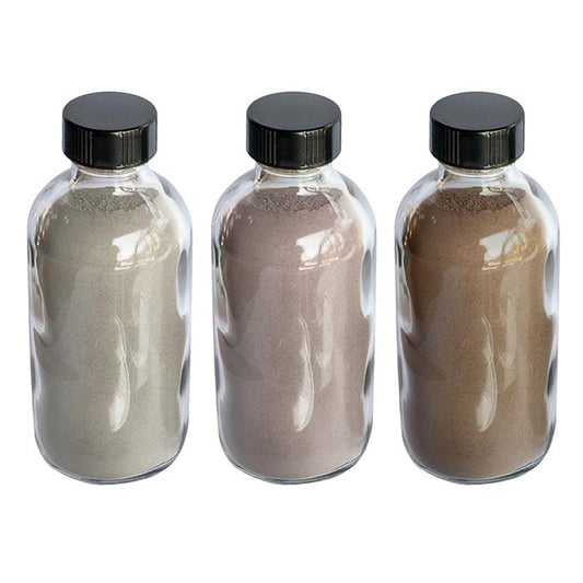 Three clear bottles with black lids containing rapé (hapé) snuff in differing shades from grey to brown on a white background