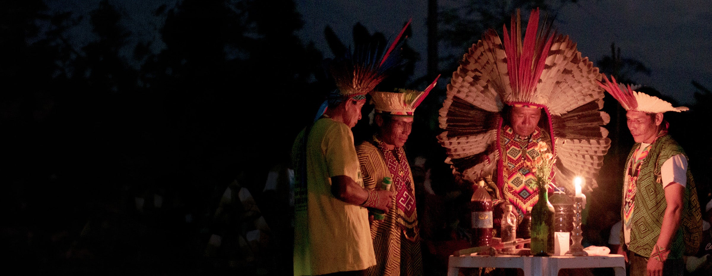 Huni Kuin elders in feathered headdresses at a candlelit ceremony in Acre